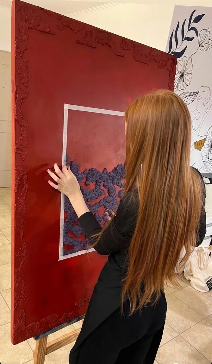 Sofía trabajando la textura de una obra roja de gran formato en el caballete