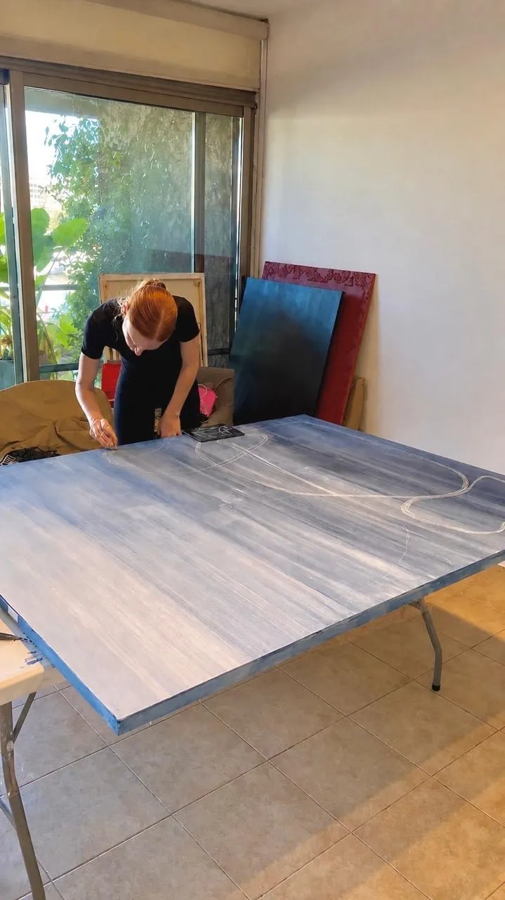 Sofía dibujando líneas sobre un lienzo azul de gran formato en su taller